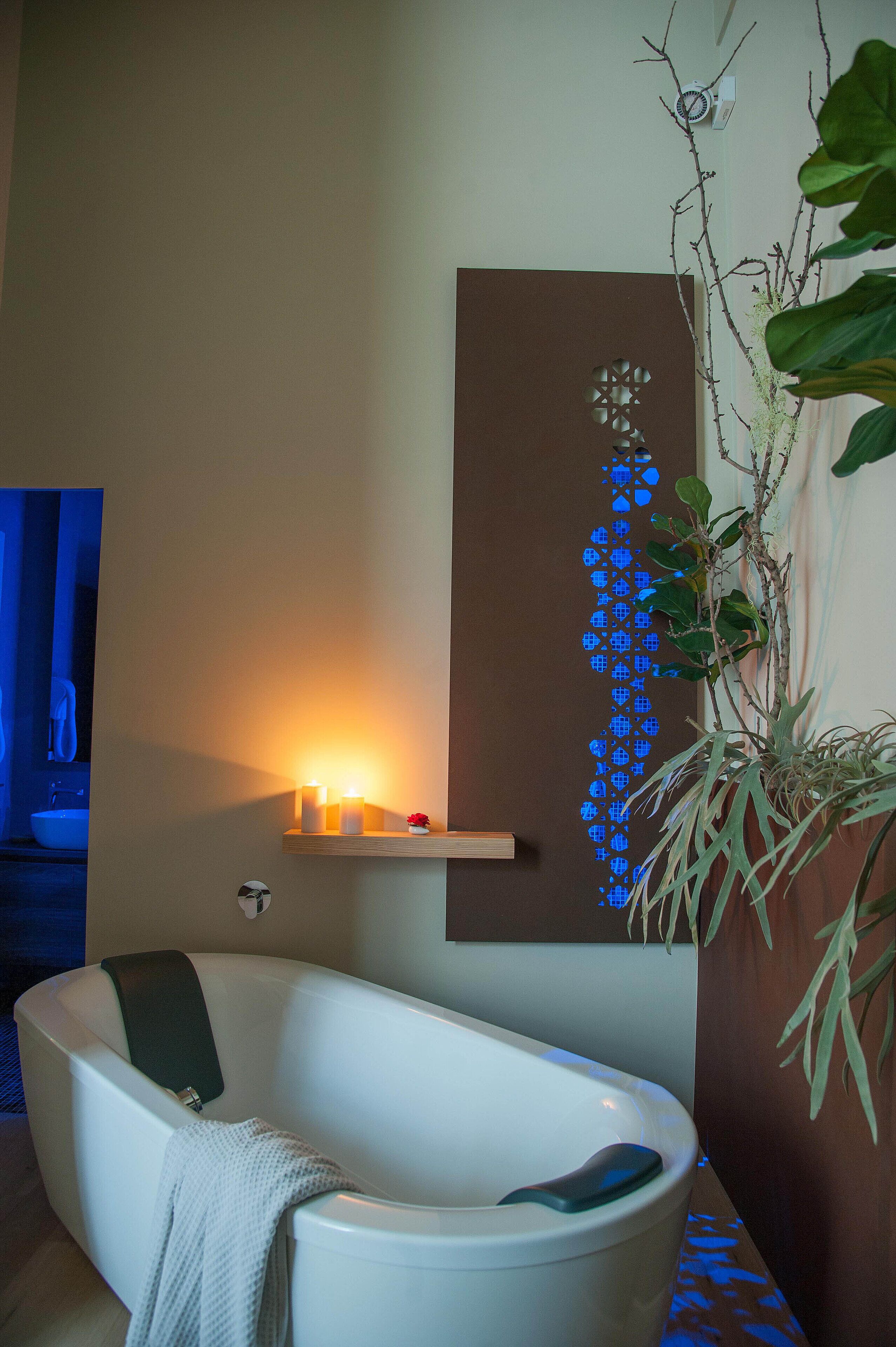 A modern bathroom with a freestanding bathtub, a wall-mounted shelf with candles, and a decorative wall piece.
