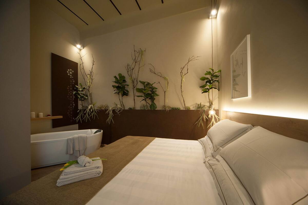A modern hotel room with a large bed, a bathtub, and wall-mounted plants.