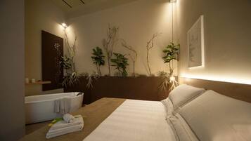 A modern hotel room with a large bed, a bathtub, and wall-mounted plants.