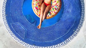 Iemand ligt op een donutvormige luchtbed in een rond zwembad met blauwe mozaïektegels.