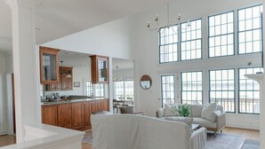 Un salon spacieux avec une grande fenêtre, une cuisine dotée de meubles en bois et un plafond haut.