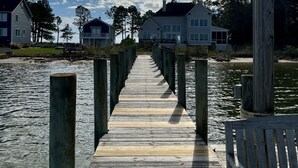 Une jetée en bois s’étendant dans une eau calme, menant à des maisons sous un ciel dégagé.