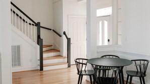 Une pièce spacieuse avec un plancher en bois, une table de salle à manger ronde entourée de chaises, un canapé en cuir marron et un escalier avec des rampes noires.