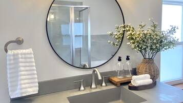Un baño con un espejo redondo, un lavabo con dos grifos, un perchero y un florero con flores.