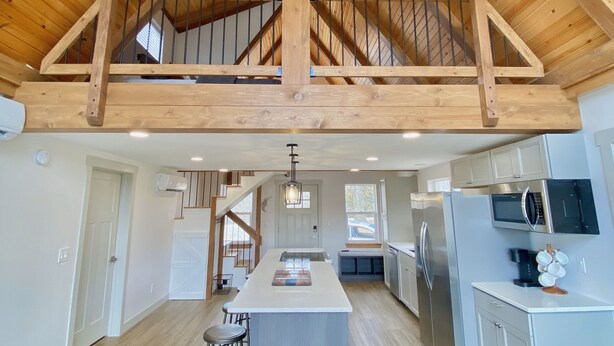A spacious kitchen with a central island, wooden ceiling beams, and a view to a second level.