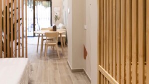 Una habitación con cama, un separador de madera, una zona de comedor con mesa y sillas, y vista por una ventana.