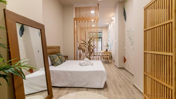 Un dormitorio con una cama, un armario de madera, un espejo y una pequeña mesa con sillas.