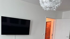 Una sala de estar moderna con un televisor de pantalla plana montado en la pared, una mesita redonda negra con un control remoto y suelo de madera.