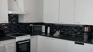 Una cocina moderna con armarios blancos, encimera negra, estufa, microondas y cafetera.