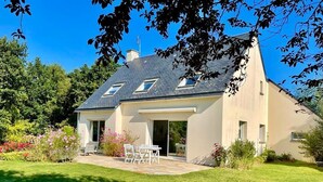 A two-story house with a sloped roof, a patio with outdoor furniture, and a well-maintained garden. - Charming villa - beaches 5 minutes away (Carolles)