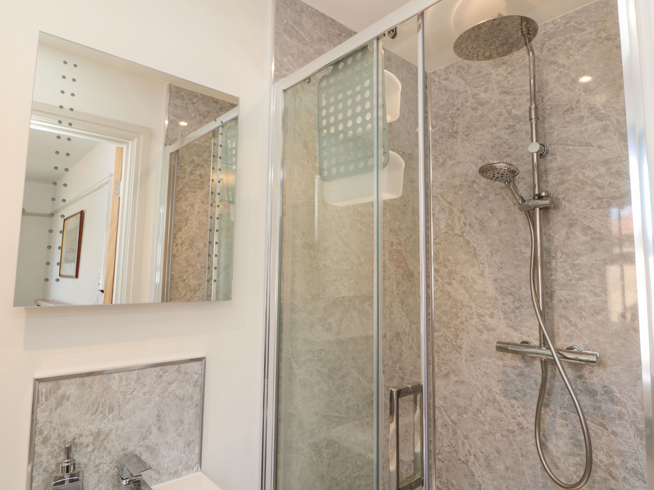 Une salle de bain moderne avec une douche à parois de verre, un grand miroir et des murs en marbre.