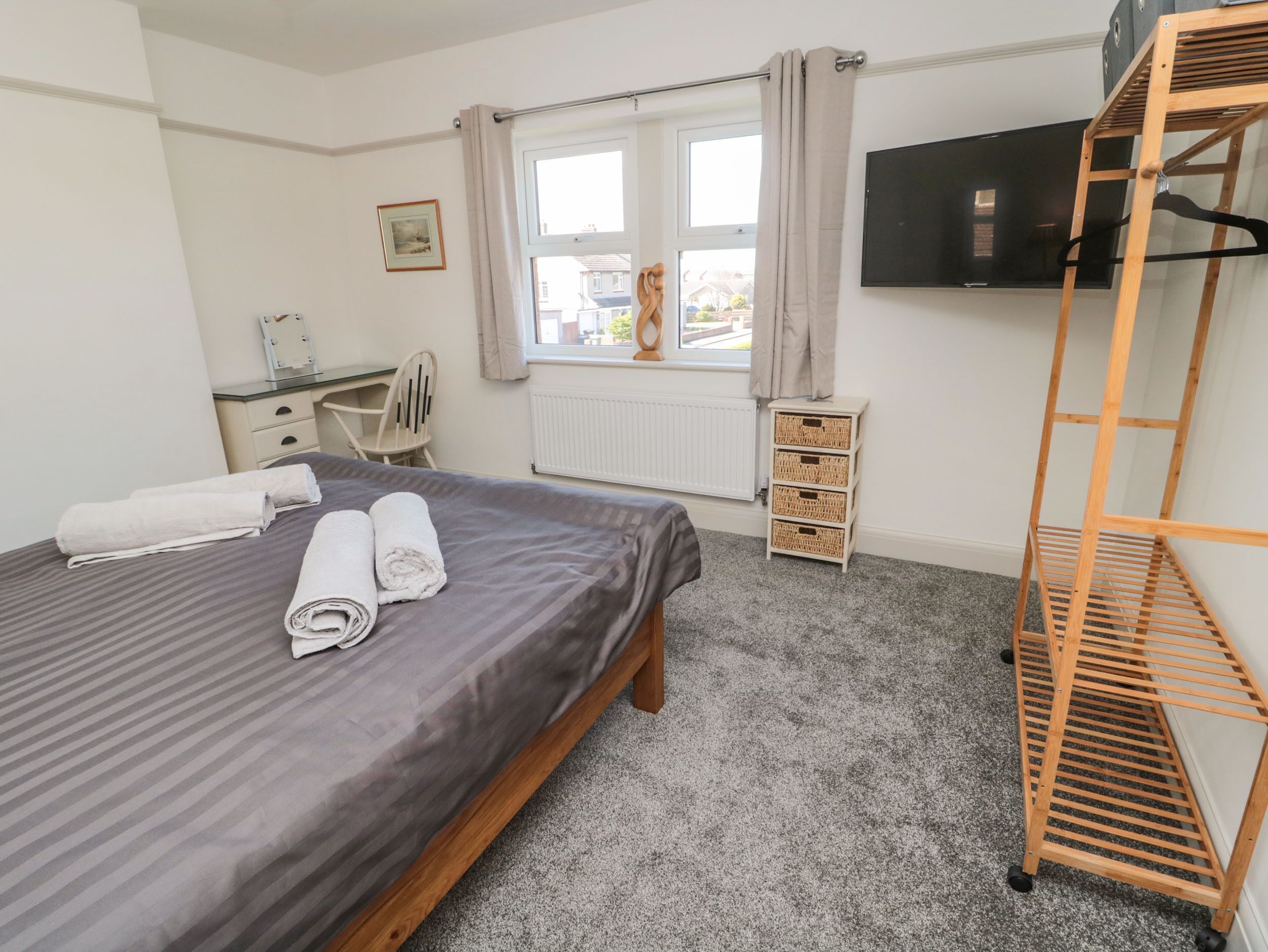A hotel room with a bed, a desk, a chair, a TV, and a wooden shelf.