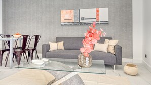 A modern living room with a grey sofa, a glass coffee table, and a vase with pink flowers.