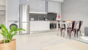 A modern kitchen with white cabinets, stainless steel appliances, and a dining area with a glass table and metal chairs.
