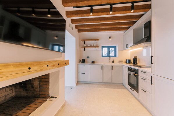 A modern kitchen with white cabinets, a built-in oven, and a brick fireplace. - Kalathos Square Luxury Suites (Rhodes)