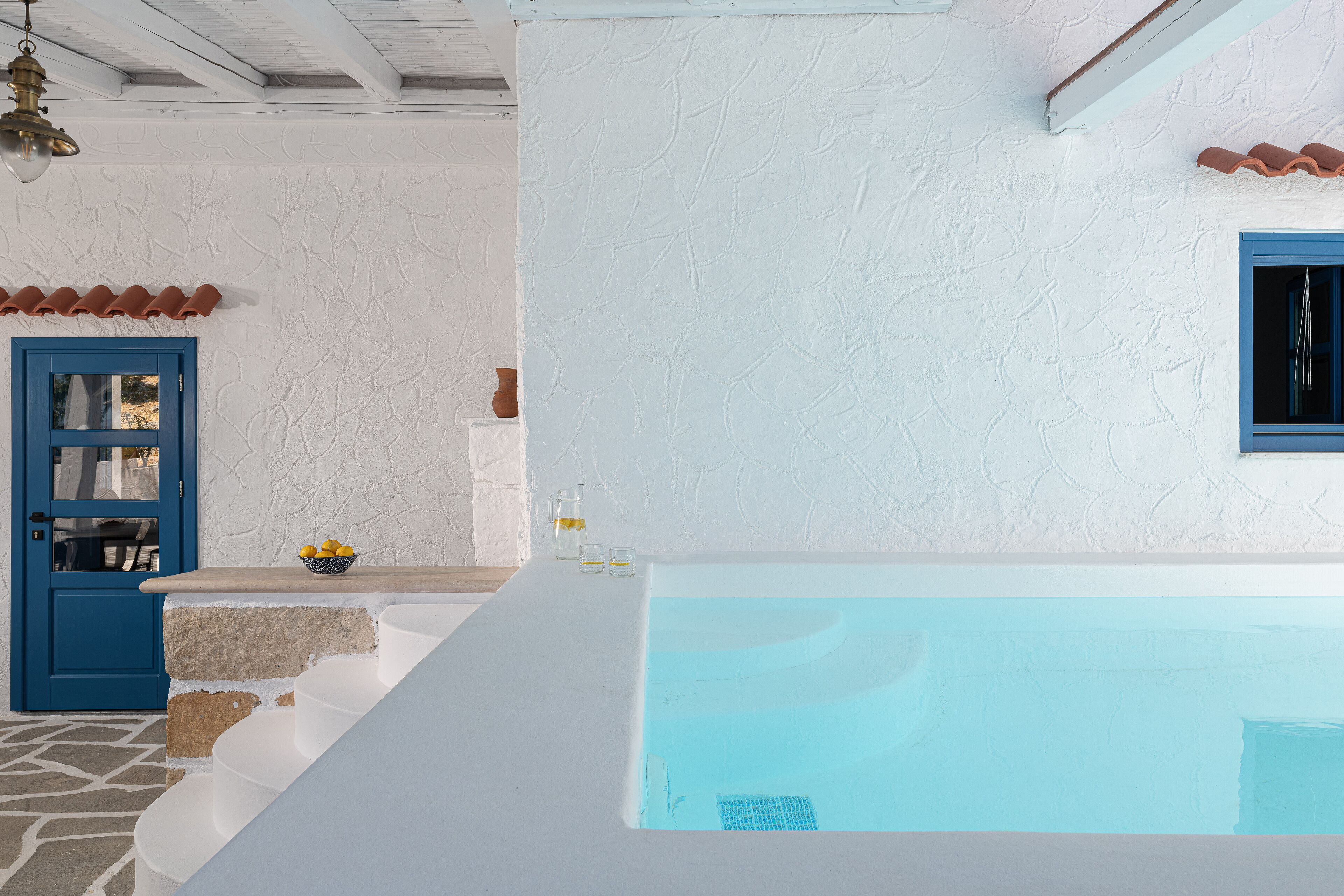 Una habitación con paredes blancas, una puerta azul, una bañera y una mesita con limones y vasos.