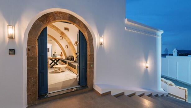 Un interior moderno con un arco de piedra que conduce a un comedor, una escalera y vistas al mar.