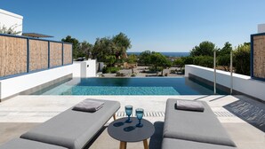 Un área de piscina moderna al aire libre, con dos sillones y una mesa, con vistas a un paisaje pintoresco.