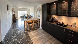 Una cocina moderna con armarios oscuros, suelo de mármol y un comedor con mobiliario de madera.