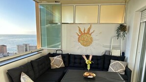 Un balcón con un sofá negro, una pequeña mesa con adornos y un mural en la pared con un sol.