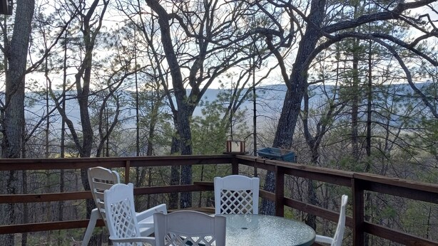 Une terrasse en bois avec une table ronde et deux chaises, donnant sur une zone boisée avec des montagnes en arrière-plan.