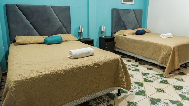 Two single beds with headboards, a small bedside table with a lamp, and a neatly folded towel on each bed. - Atitlans House  (Panajachel)
