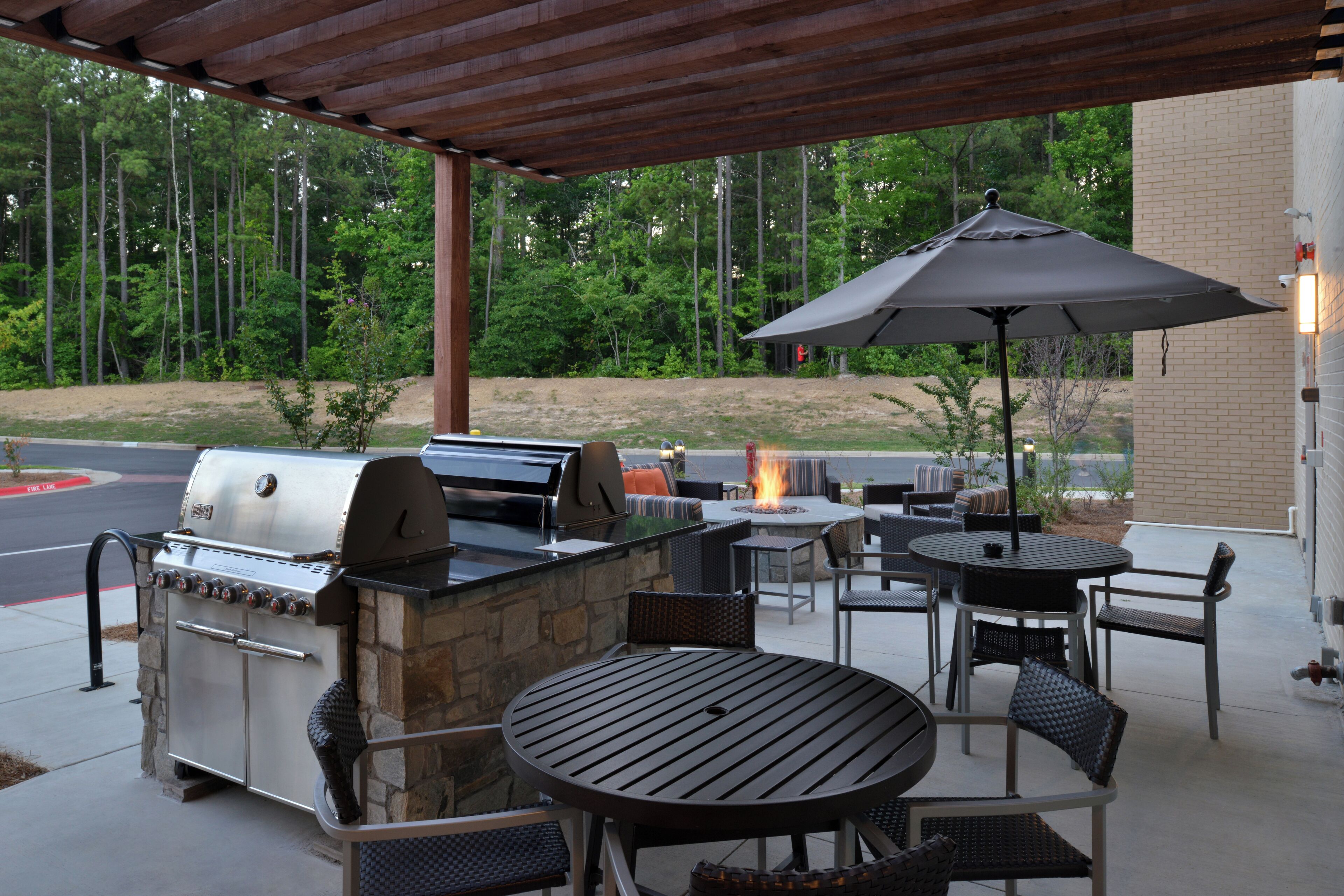 An outdoor patio with a stone barbecue, wicker furniture, and a fire pit.