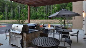 An outdoor patio with a stone barbecue, wicker furniture, and a fire pit.