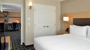 A hotel room with a bed, a desk, and a chair. There is a door and a wall-mounted lamp.