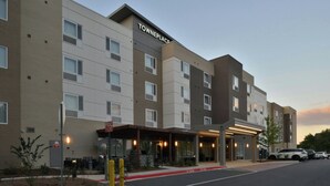 A multi-story hotel with a 'TOWNEPLACE' sign, a covered entrance, and a parking area with cars.