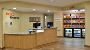 A reception area with a wooden counter, a 'HELLO Morrisville' sign, a 'PINCH' sign above a snack display, and a 'Manager on Duty' sign.