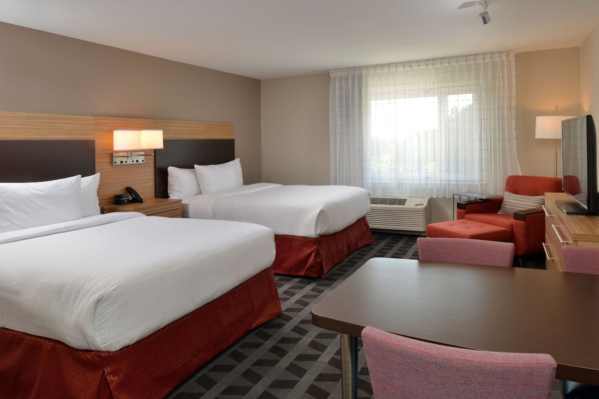 Une chambre d’hôtel avec deux lits, un bureau, une chaise, une télévision et une fenêtre avec des rideaux.
