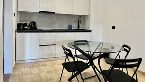 A compact kitchen with white cabinets, a black countertop, and a glass dining table with four chairs. - STAY Napa Velvet (Ayia Napa)