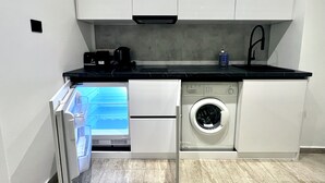 A compact kitchen with integrated appliances including a washing machine, a coffee maker, and a built-in oven. - STAY Napa Velvet (Ayia Napa)