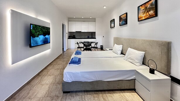 A modern hotel room with a large bed, a TV mounted on the wall, a dining area, and artwork on the walls. - STAY Napa Velvet (Ayia Napa)