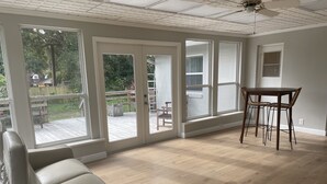 Ein geräumiges Zimmer mit großen Fenstern, einer Holzterrasse und einem Essbereich.