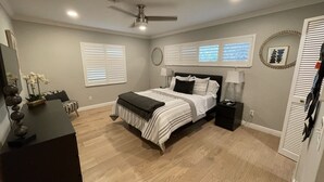 Ein Schlafzimmer mit Bett, Nachttischen, Deckenventilator und einem Fenster mit Jalousien.