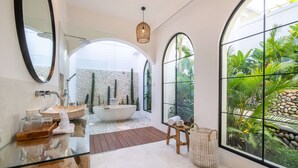 A modern bathroom with a glass vanity, a freestanding bathtub, and a large window with a view of tropical plants. - Private Pool Retreat•Ubud 1br Villa•Jungle Serenity (Ubud)
