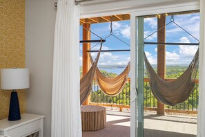 Relax in a serene room with a hammock, round bench, and stunning views of a lush landscape featuring a body of water and rolling hills.