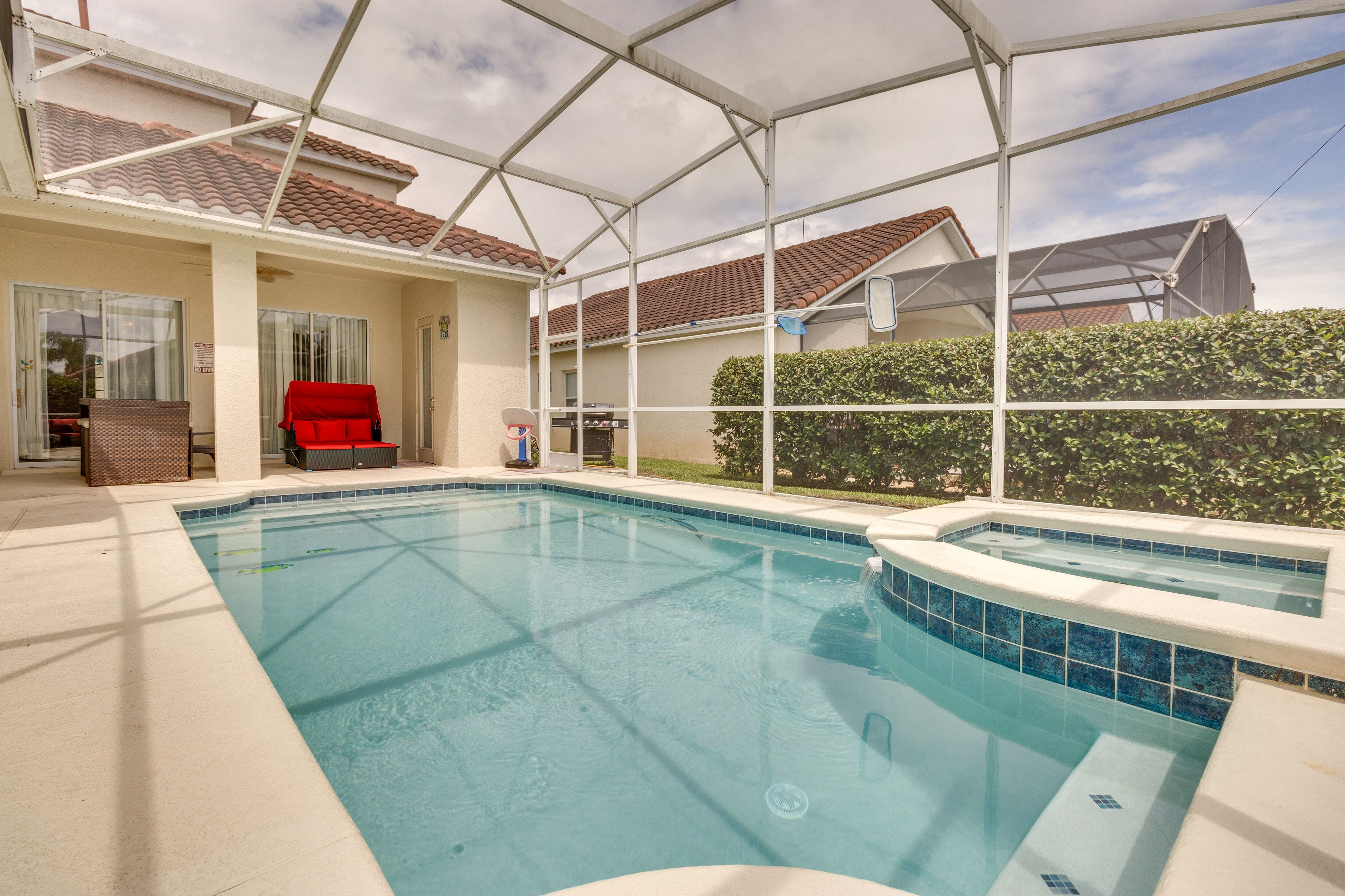 An indoor swimming pool with a covered patio area, a red chair, and a barbecue grill.