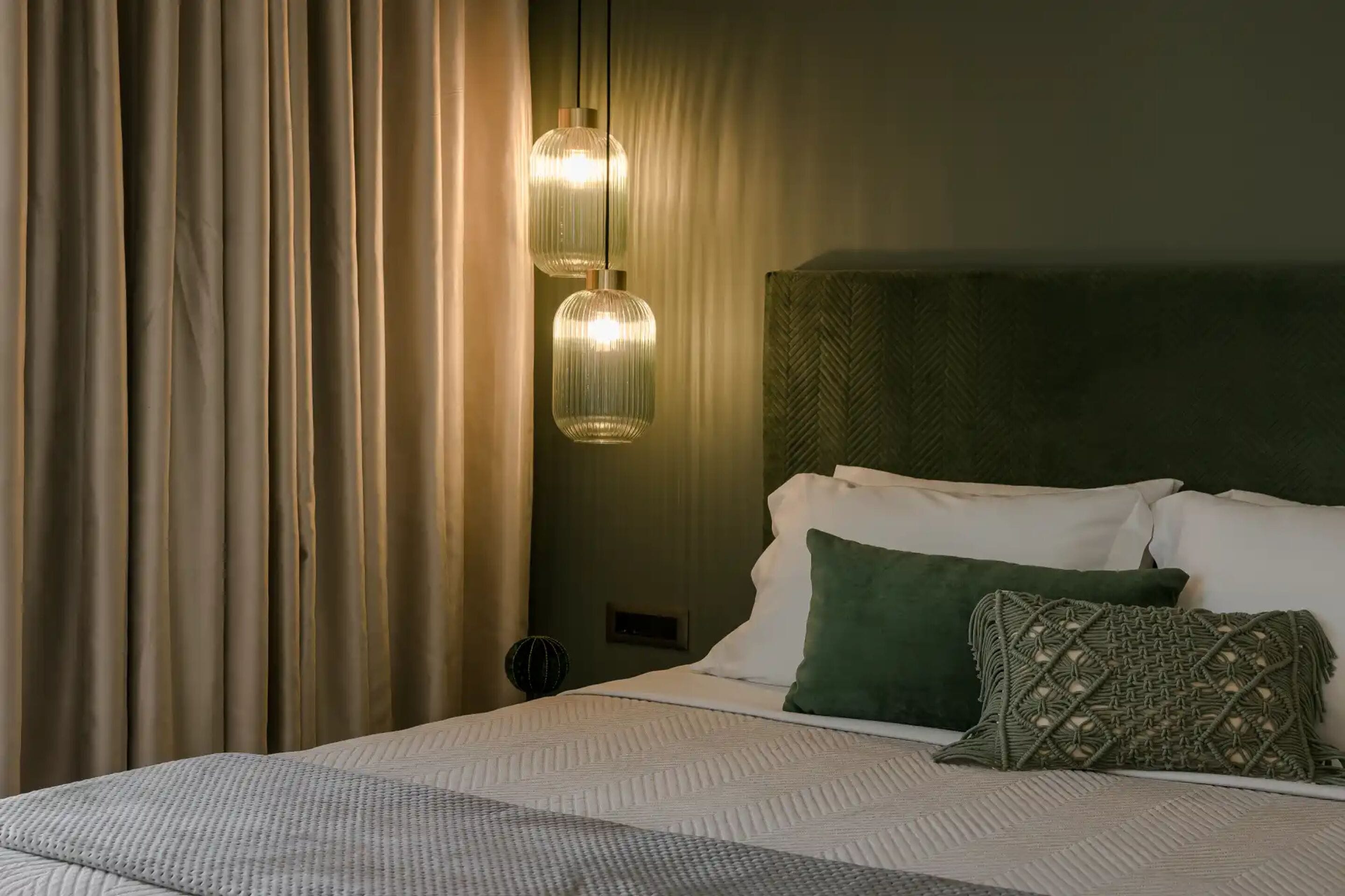 A neatly made bed with white and green pillows, a textured blanket, and two hanging pendant lights.