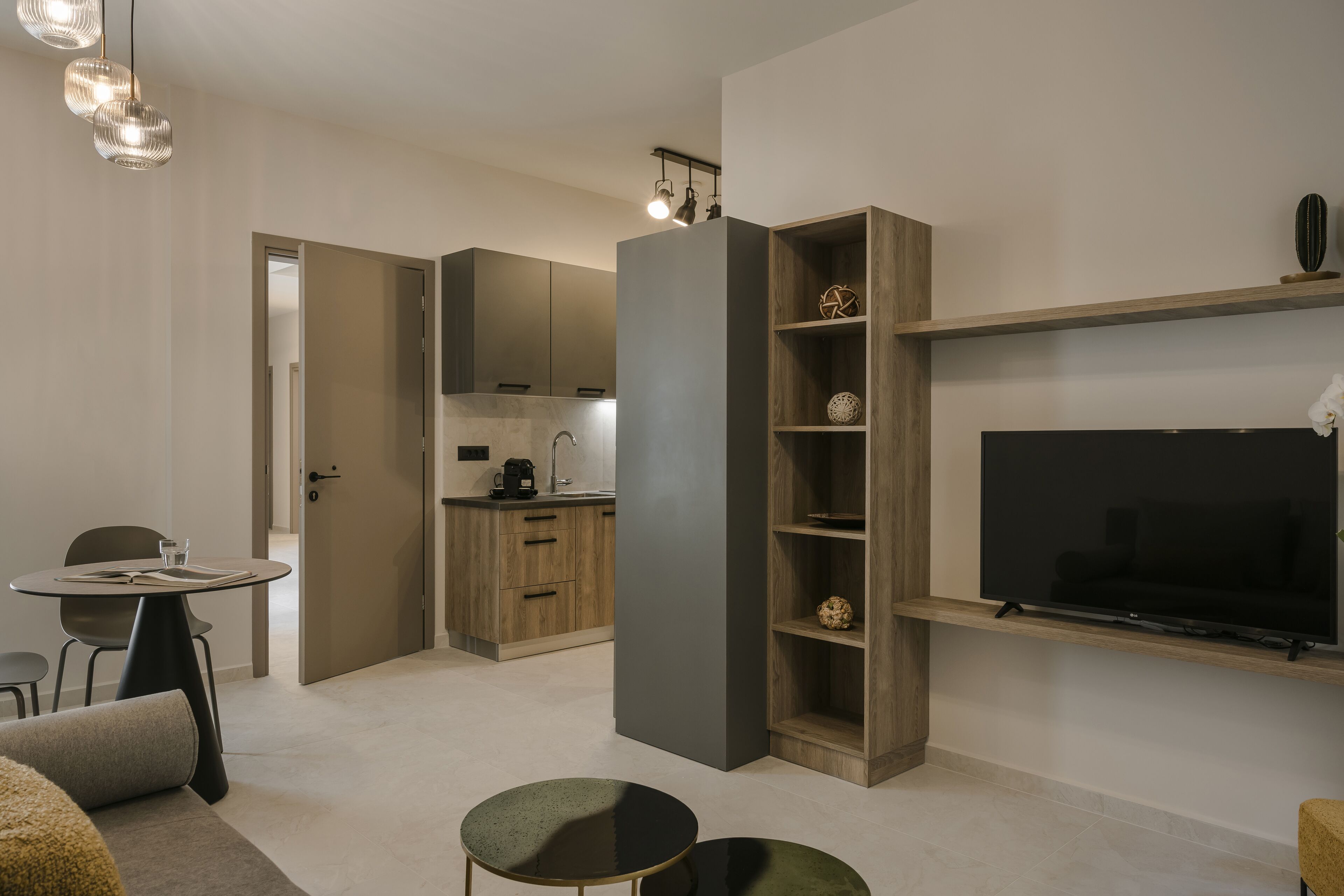 Een moderne woonkamer met een flatscreen televisie, een eethoek met een tafel en stoelen, en een keuken op de achtergrond.