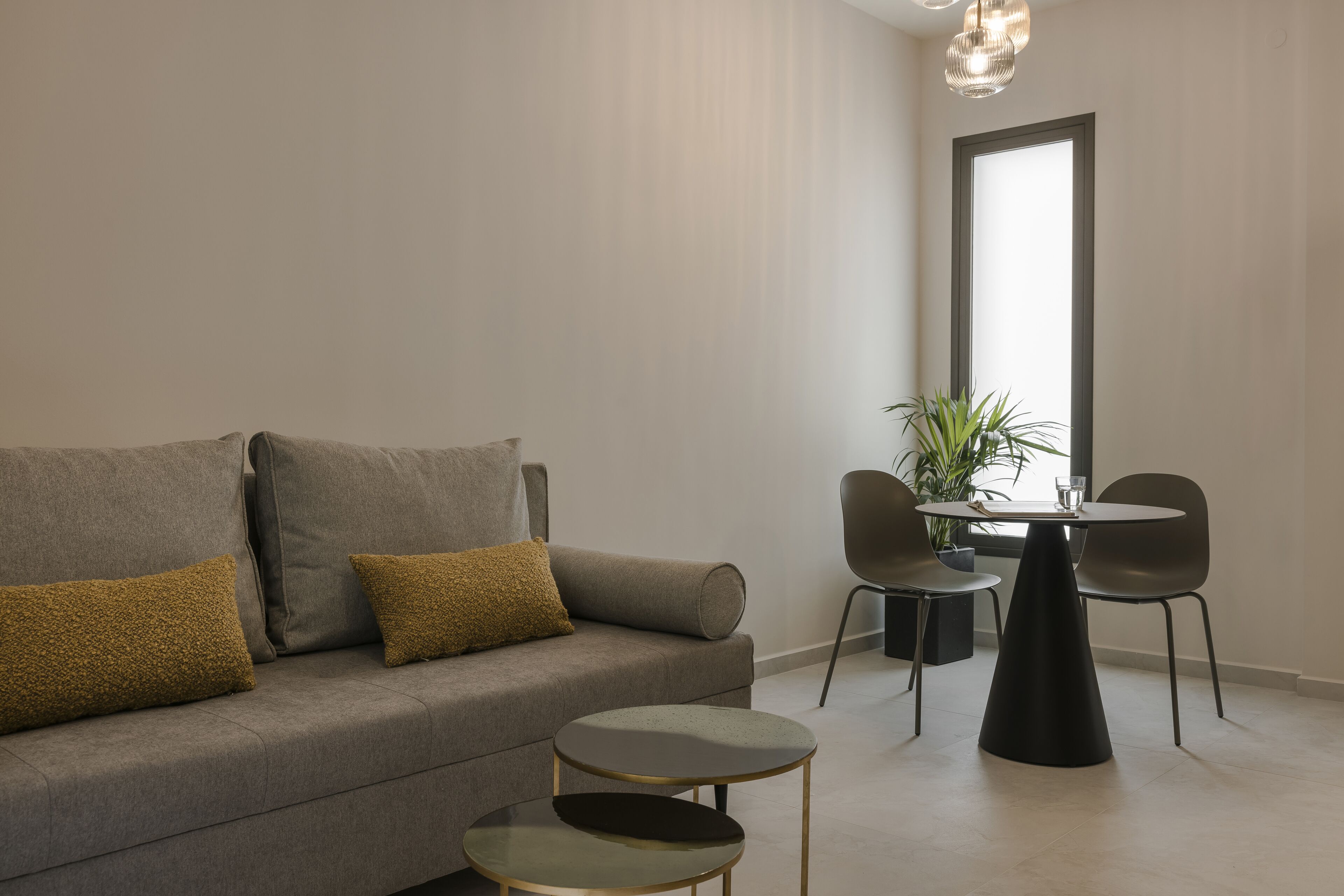Un salón moderno con un sofá gris, dos mesitas auxiliares redondas y una pequeña mesa redonda con sillas.