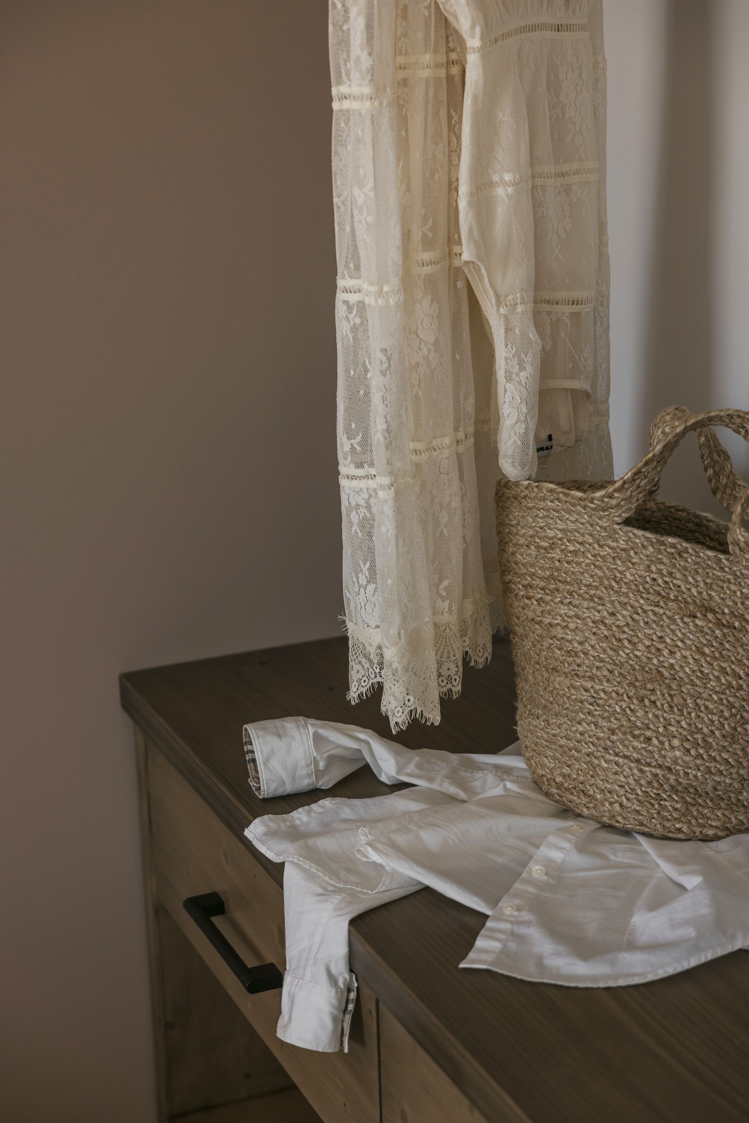 Un aparador de madera con una cesta tejida y cortinas de encaje blanco.