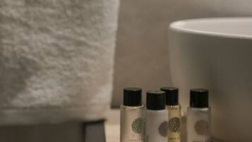 Une salle de bain avec une serviette blanche suspendue à un porte-serviettes, un lavabo et trois flacons de produits de soins corporels disposés sur un plateau.