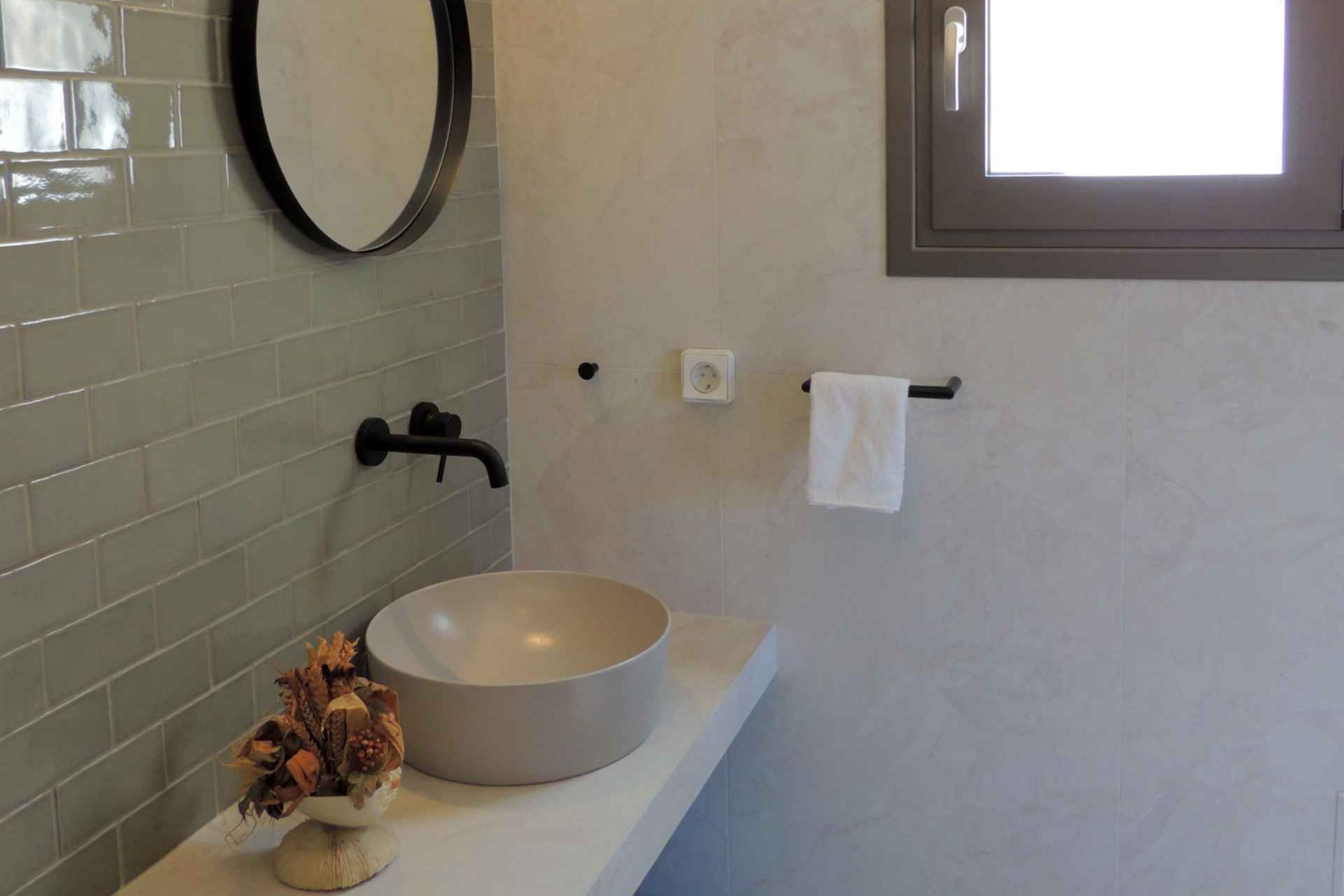 A bathroom with a round sink, a mirror, and a window.