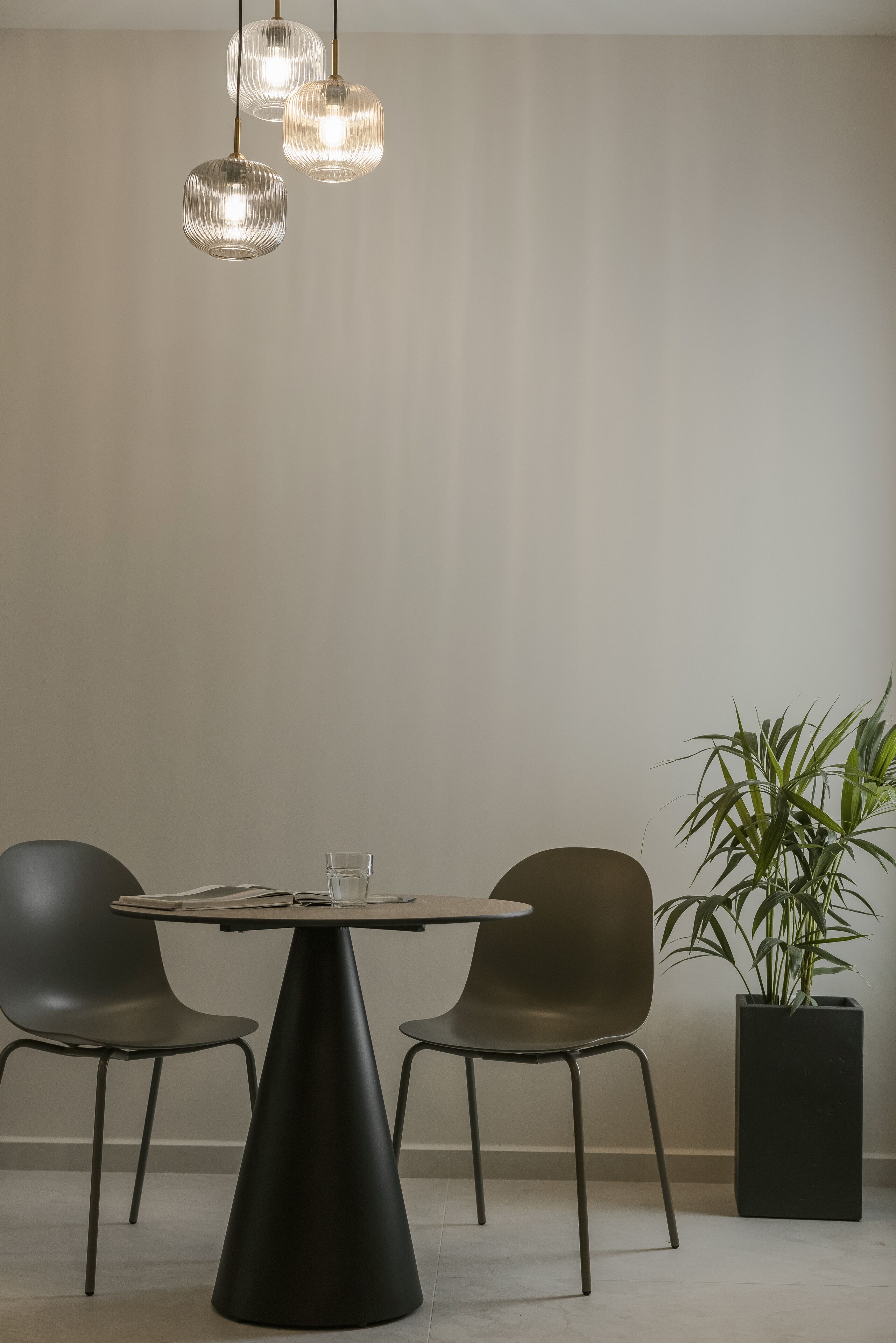 A modern dining area with a round table, two chairs, and three pendant lights.