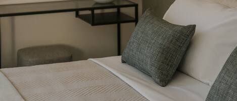 A modern bedroom with a round mirror, two pendant lights, a bedside table with a vase, and a bed with pillows.