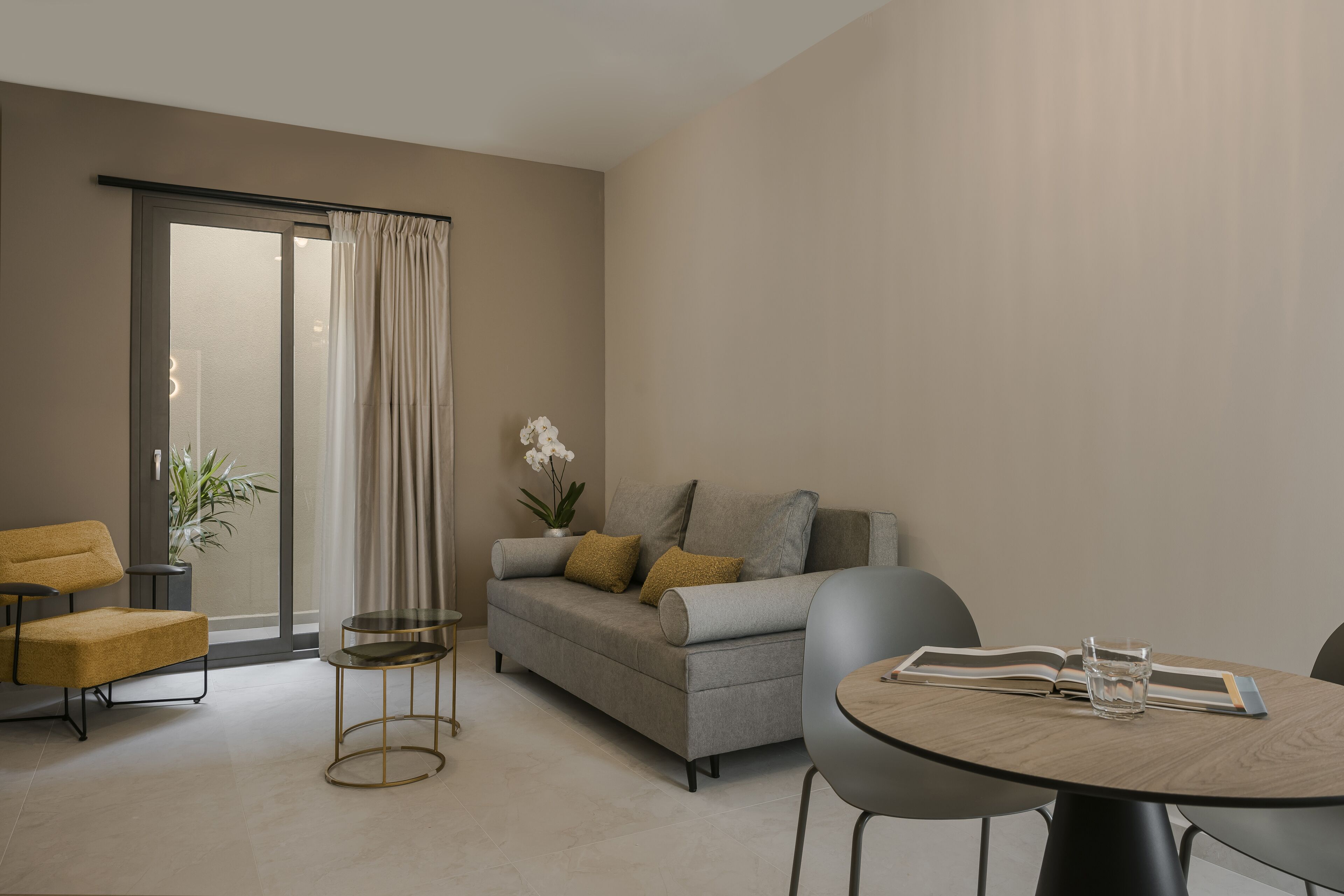 A modern living room with a sofa, a coffee table, and a chair. There is a sliding glass door leading to a balcony.