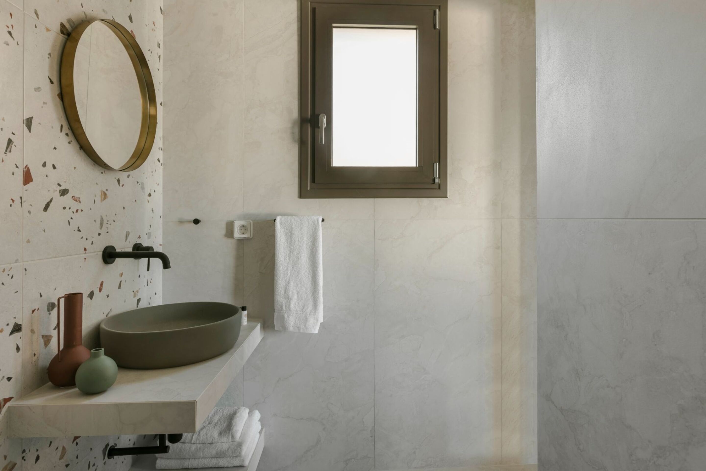 Une salle de bain avec un lavabo rond, un miroir, une serviette et une fenêtre.
